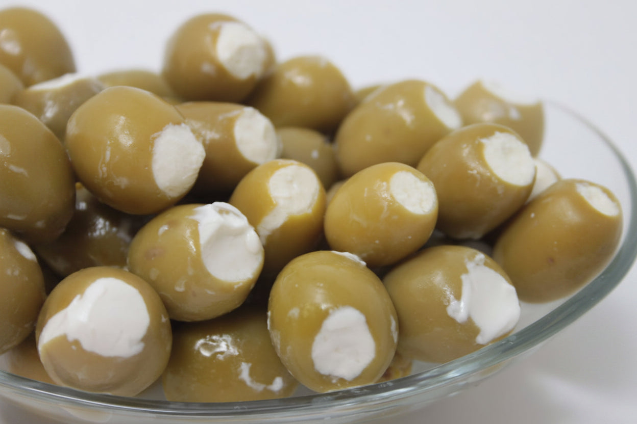 A glass bowl containing green olives hand-filled with goat cheese.